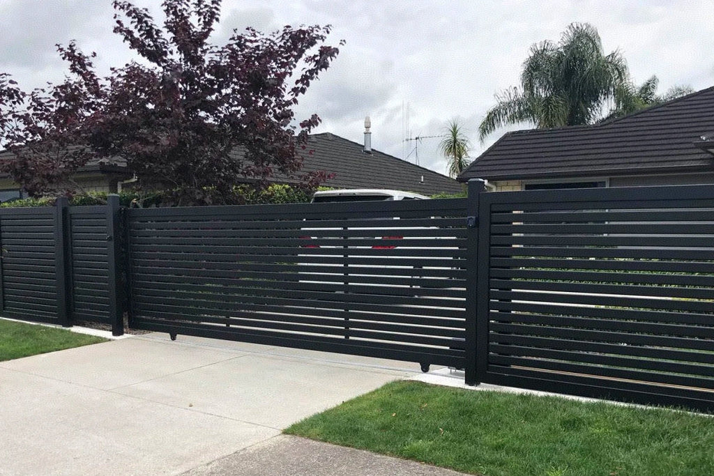 Black metal gate in a residential area with houses and trees in the background.
